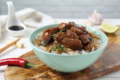 Bowl with pieces of soy sauce chicken and noodle on white table, closeup