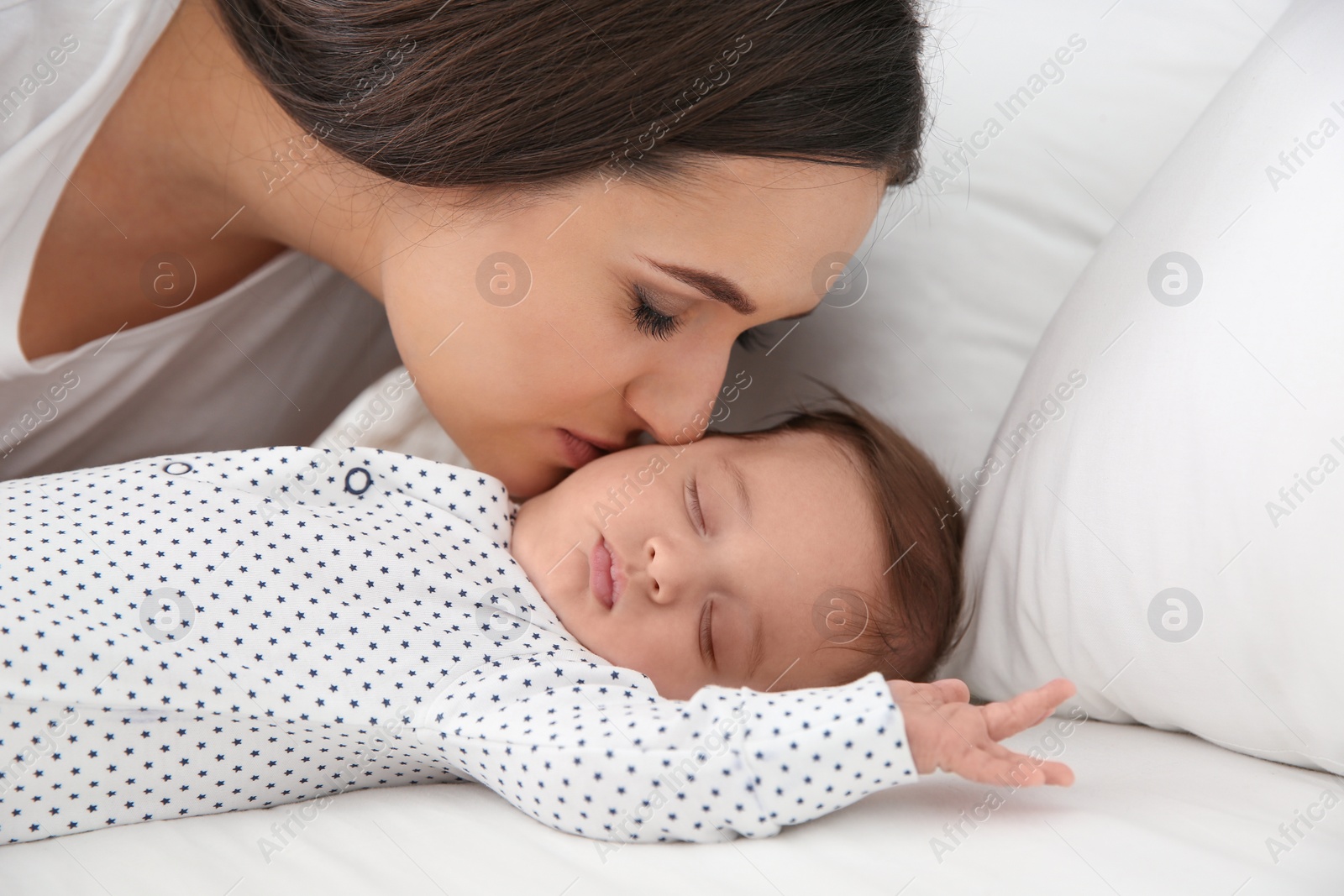 Photo of Woman kissing her sleeping baby on bed