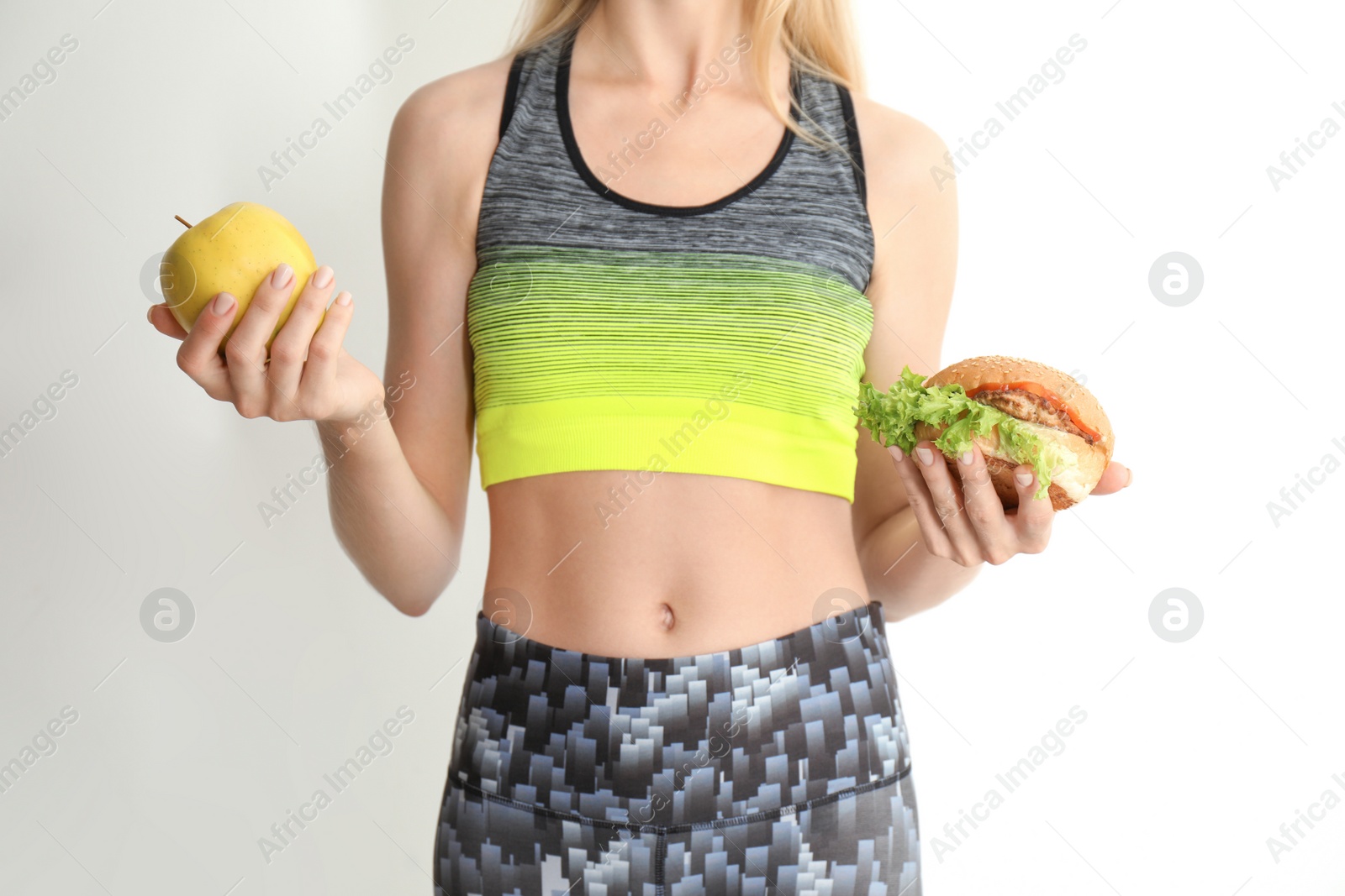 Photo of Woman holding tasty sandwich and fresh apple on light background. Choice between diet and unhealthy food