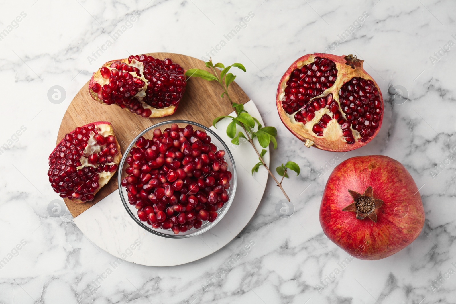 Photo of Ripe juicy pomegranate grains and green leaves on white marble table, flat lay