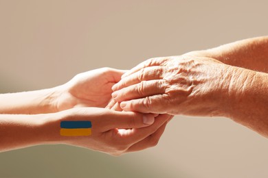 Image of Help for Ukraine. People holding hands with drawing of Ukrainian flag on light background, closeup