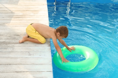 Little child reaching for inflatable ring in outdoor swimming pool. Dangerous situation