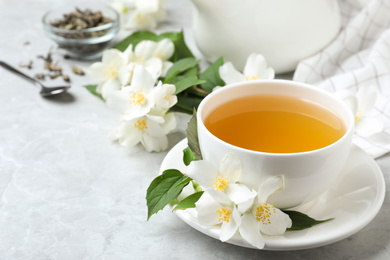 Photo of Cup of tea and fresh jasmine flowers on light grey marble table