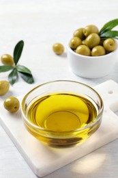 Photo of Glass bowl with fresh olive oil on white wooden table