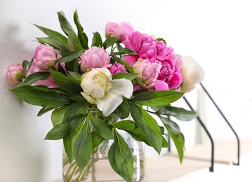 Photo of Shelf with vase of beautiful peonies on white wall