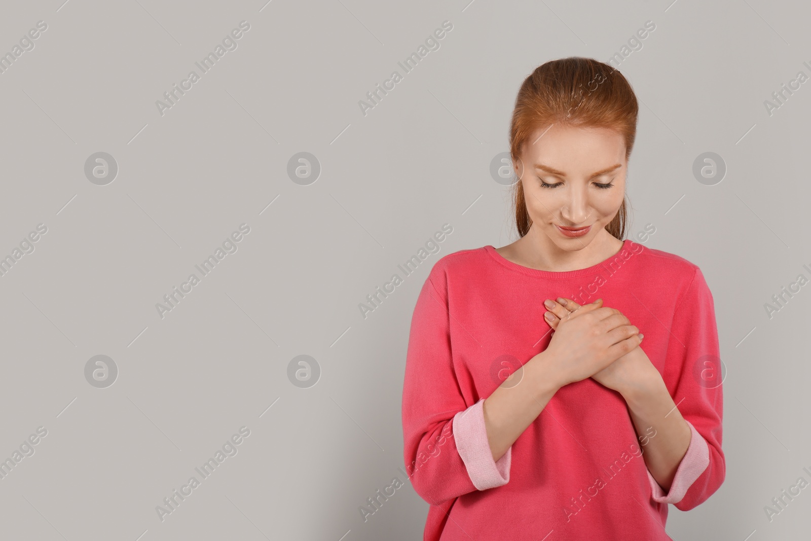 Photo of Beautiful grateful woman with hands on chest against light grey background. Space for text