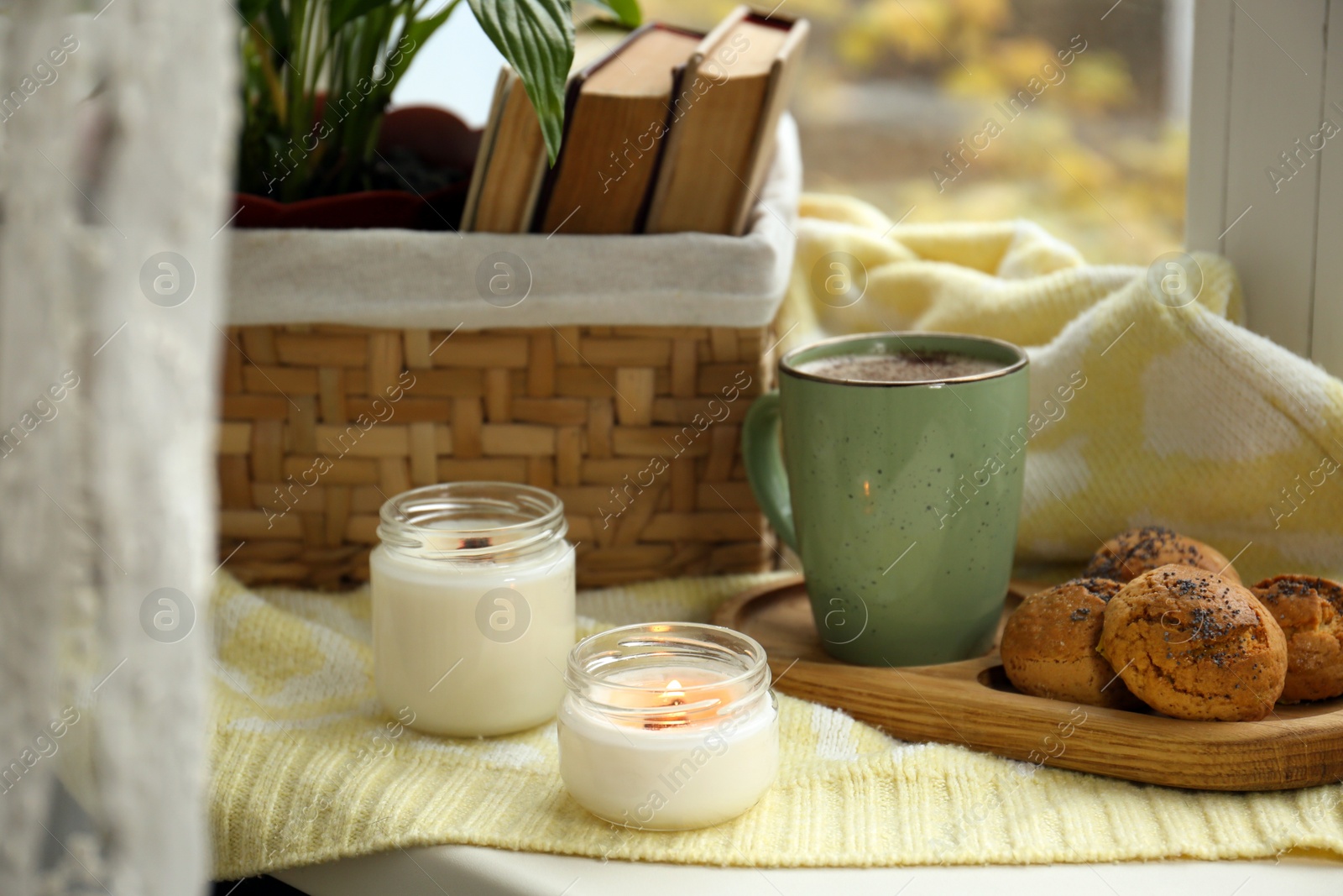 Photo of Burning aromatic candles, cup with hot drink and cookies on windowsill indoors. Autumn coziness