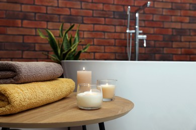 Photo of Stylish bathroom interior with ceramic tub, burning candles and terry towels on wooden coffee table. Space for text