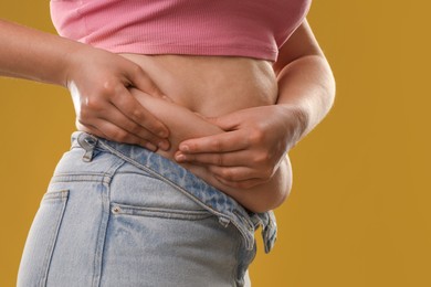 Photo of Woman touching belly fat on goldenrod background, closeup. Overweight problem
