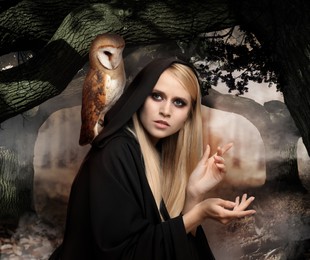 Image of Witch wearing black mantle with owl in foggy forest. Fantasy world