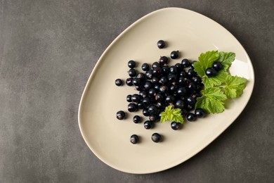 Photo of Plate with ripe blackcurrants and leaves on grey background, top view. Space for text