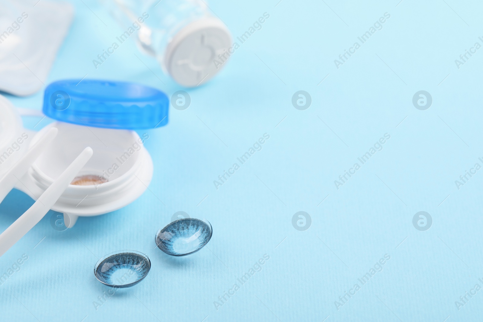 Photo of Case with color contact lenses and tweezers on light blue background, closeup. Space for text