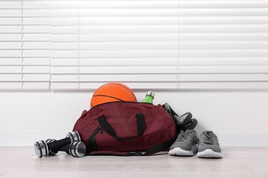 Photo of Gym bag and sports equipment on floor indoors