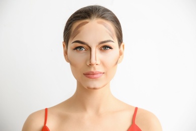 Photo of Young woman with contouring lines on her face against light background. Professional makeup products