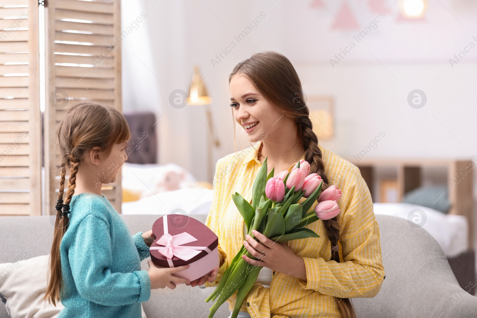 Photo of Happy mother and daughter with flower bouquet and gift at home. International Women's Day