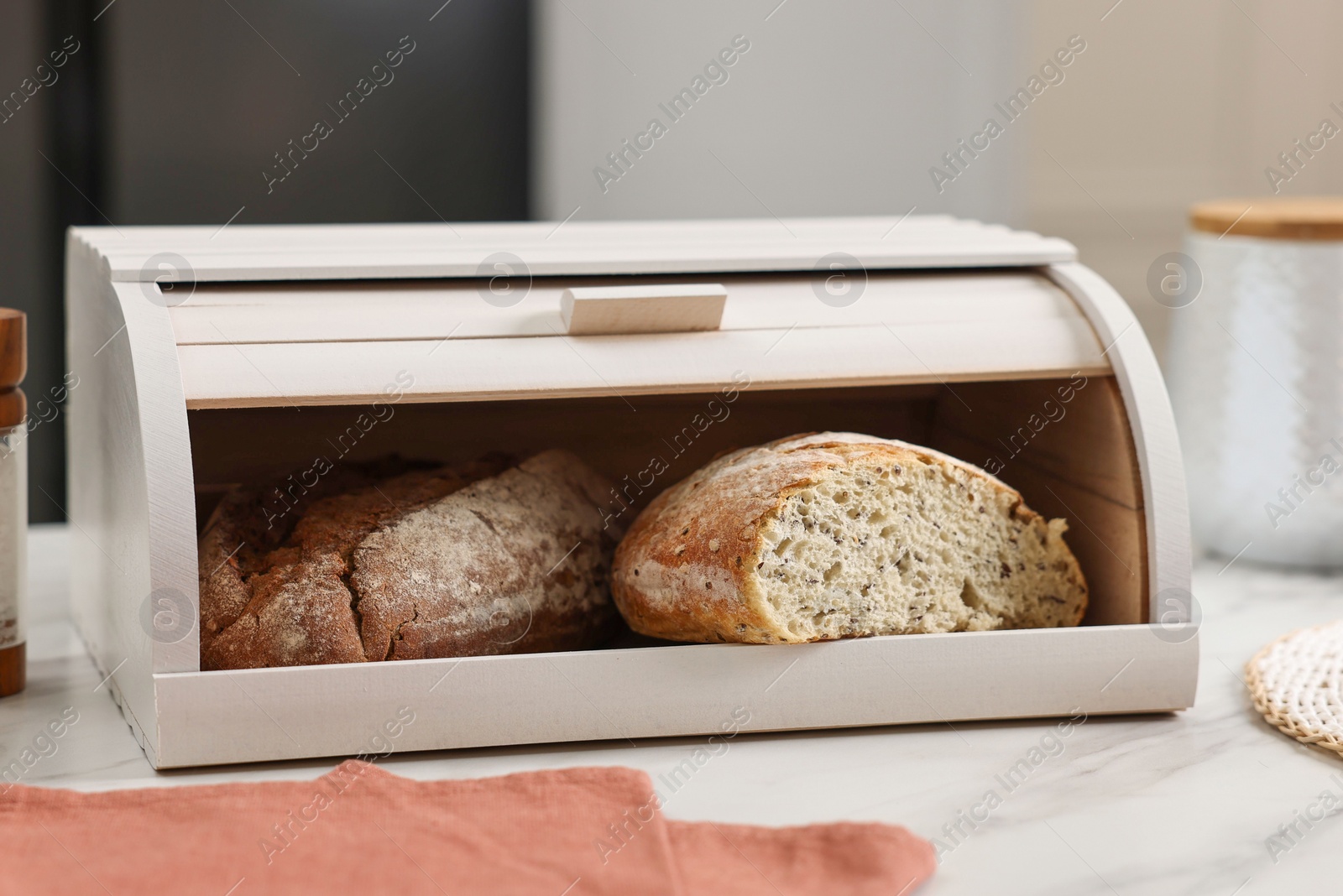 Photo of Wooden bread basket with freshly baked loaves on white marble table in kitchen