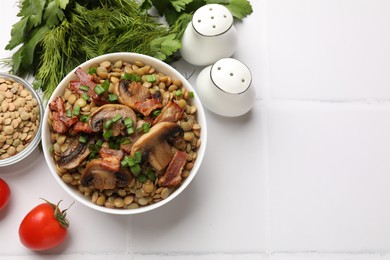 Delicious lentils with mushrooms, bacon and green onion in bowl served on white tiled table, flat lay. Space for text