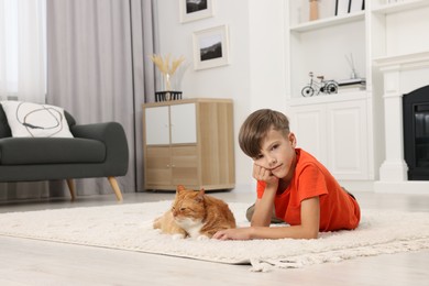 Photo of Little boy and cute ginger cat on soft carpet at home