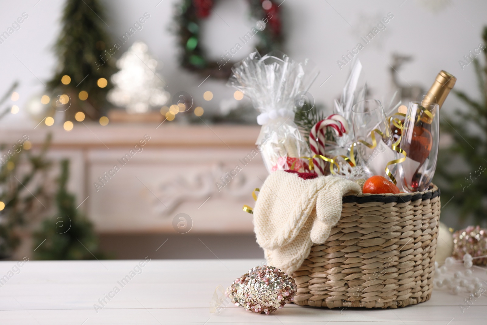 Photo of Wicker basket with Christmas gift set on white table. Space for text