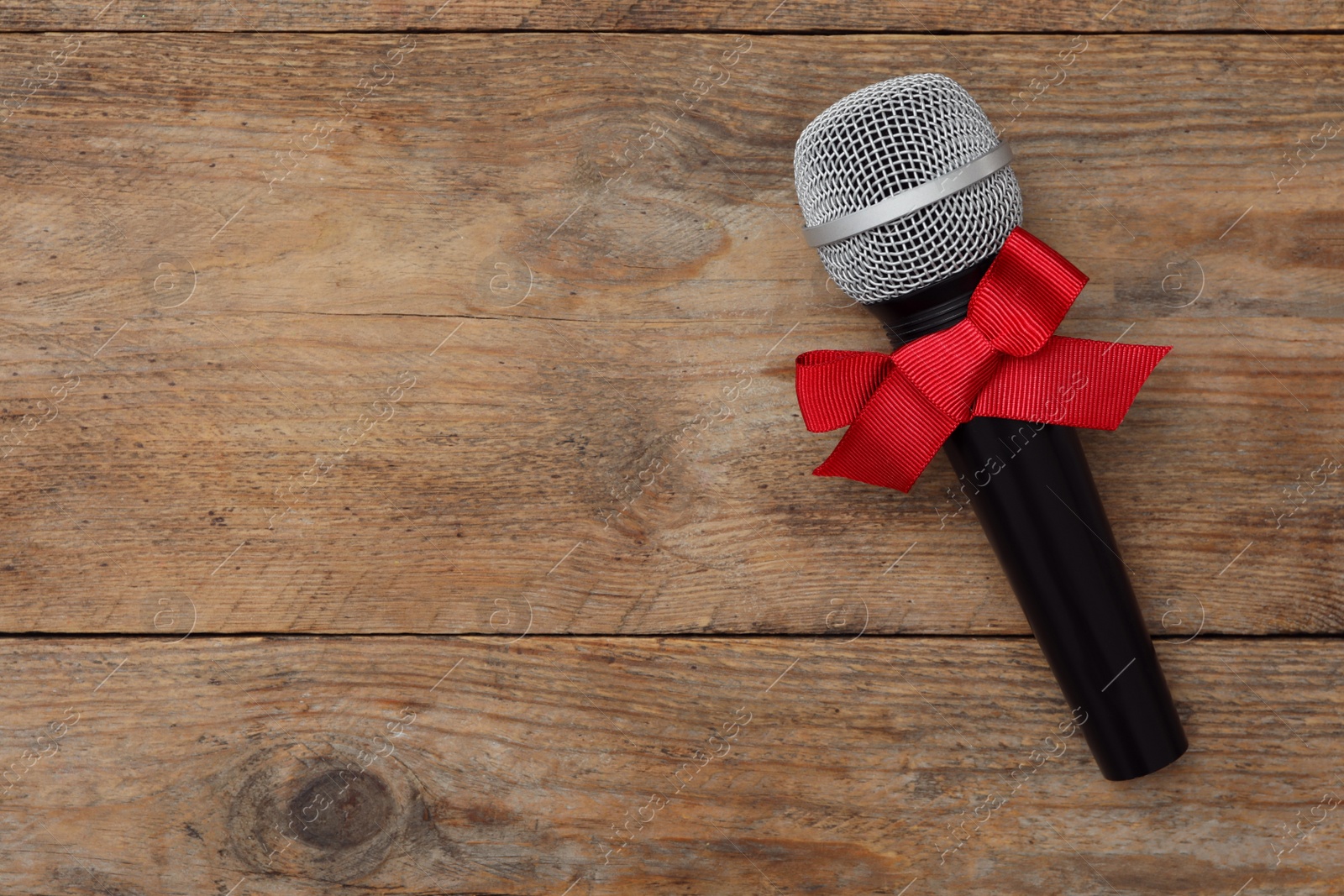 Photo of Top view of microphone with red bow on wooden table, space for text. Christmas music