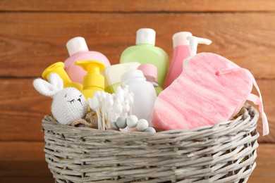 Photo of Wicker basket full of different baby cosmetic products, accessories and toys on wooden background, closeup