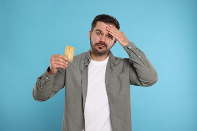 Confused man with credit card on light blue background. Debt problem