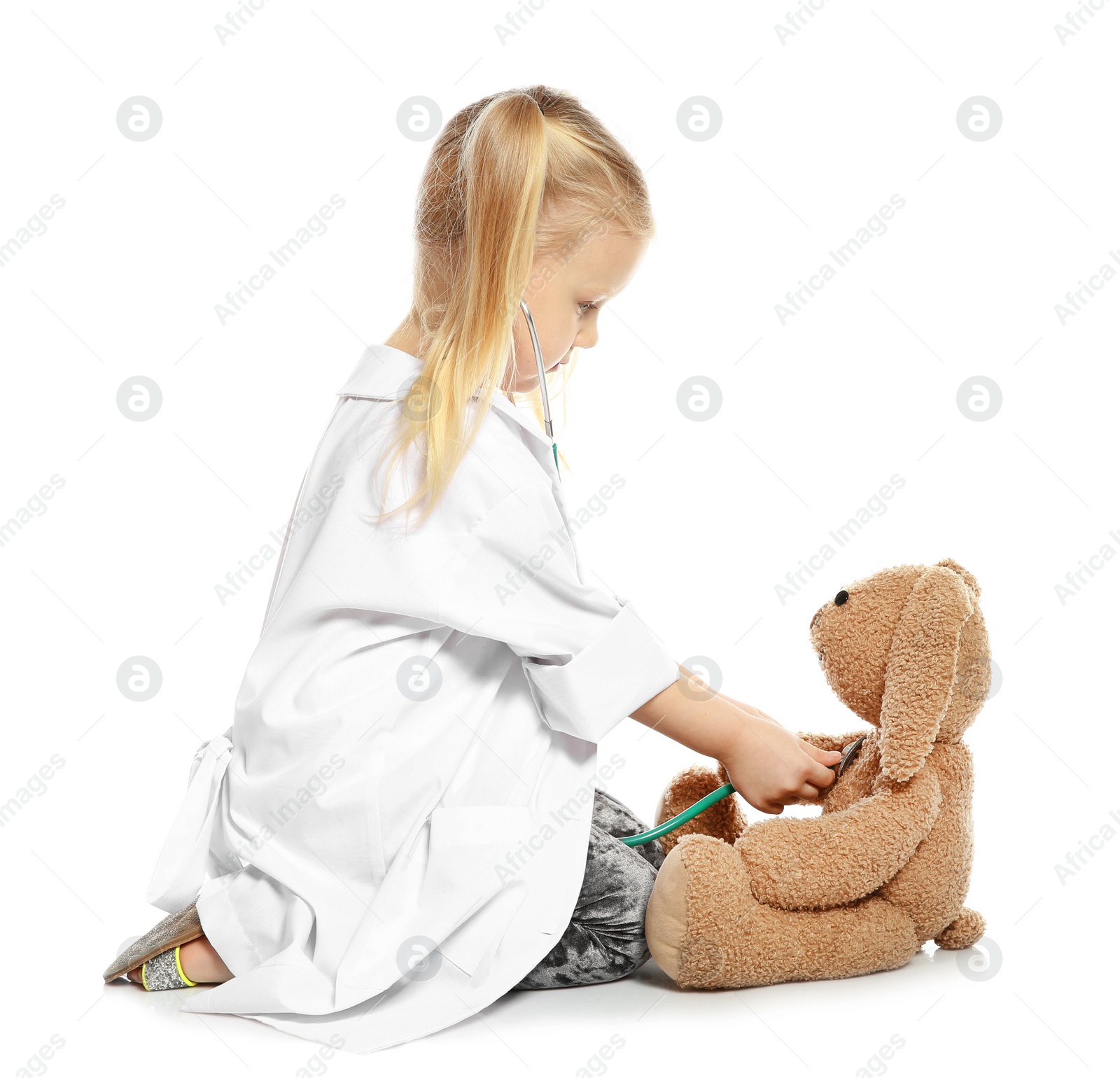 Photo of Cute child imagining herself as doctor while playing with stethoscope and toy bunny on white background