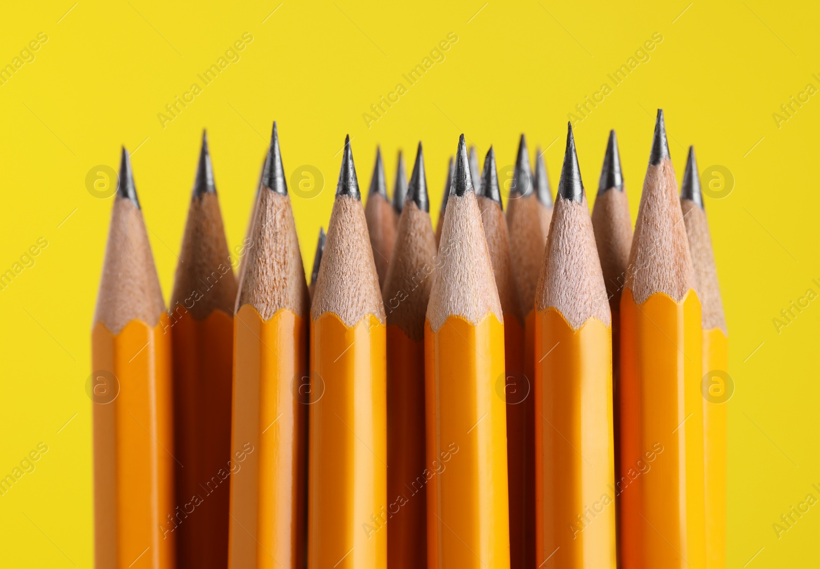 Photo of Many graphite pencils on yellow background, macro view