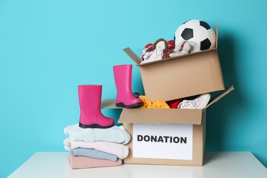 Donation boxes with toys, knitted clothes and shoes on table against color background