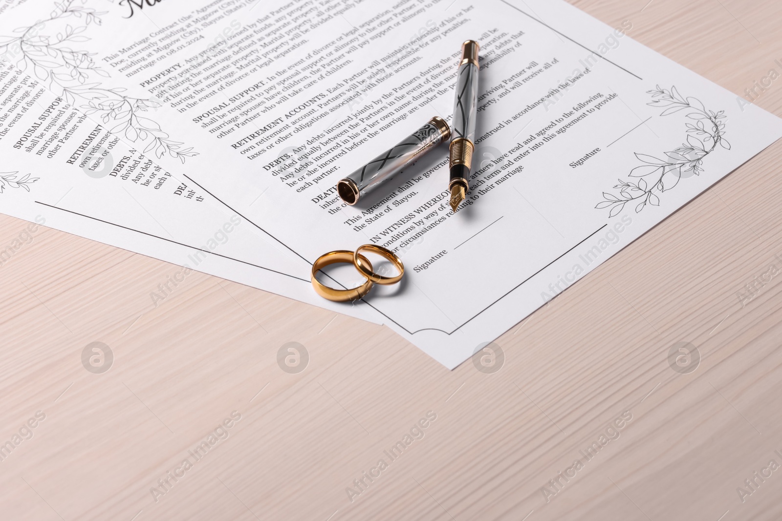 Photo of Marriage contracts, gold rings and pen on light wooden table, space for text