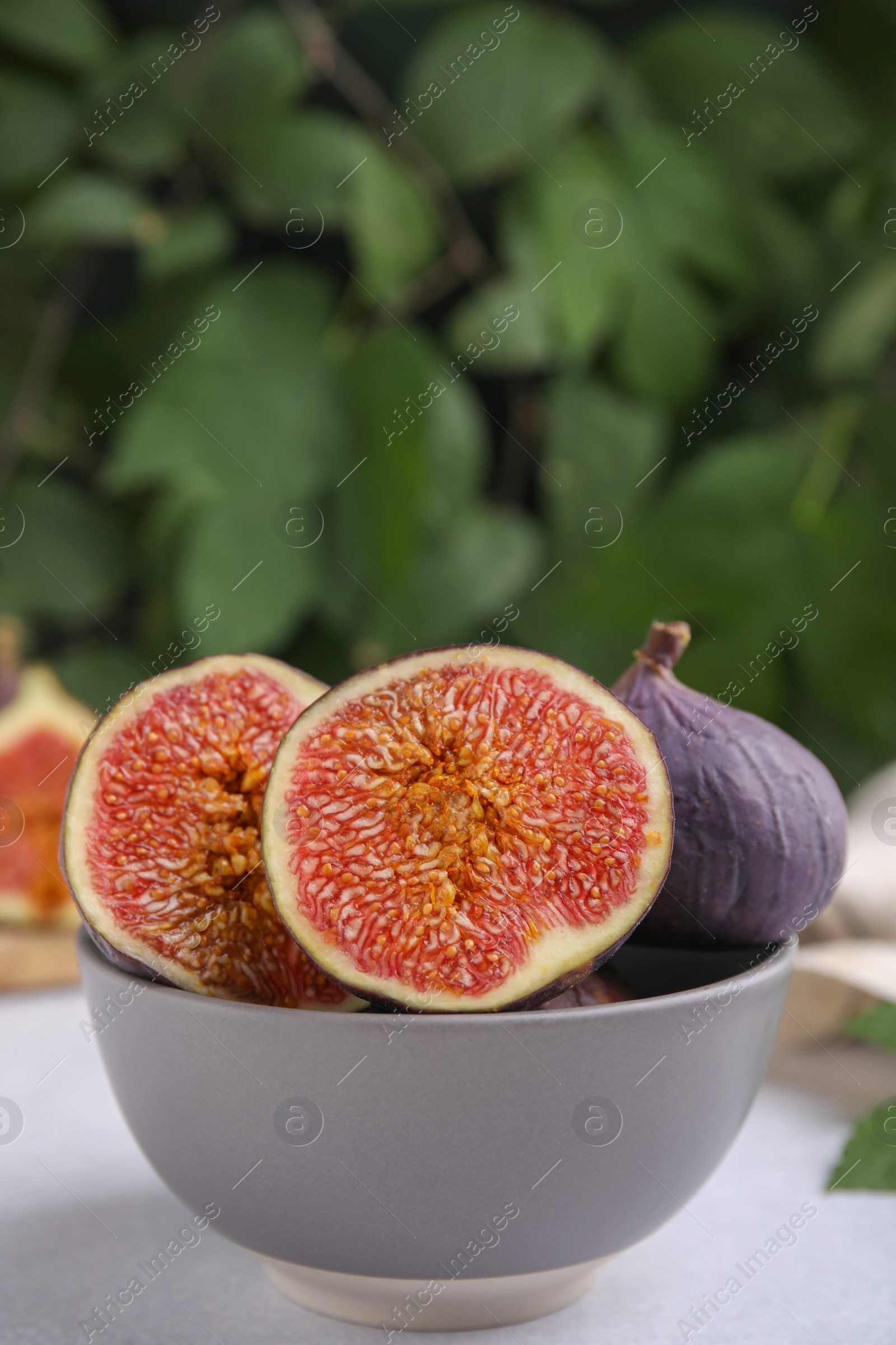 Photo of Bowl of tasty ripe figs on light table against blurred background,