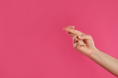 Photo of Woman holding fingers crossed on pink background, closeup with space for text. Good luck superstition
