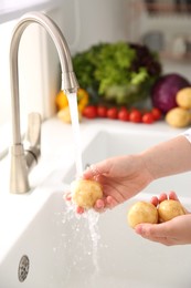 Woman washing fresh potatoes in kitchen sink, closeup