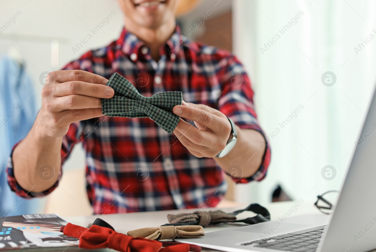 Photo of Fashion blogger with bow tie and laptop at table indoors, closeup. Online broadcast