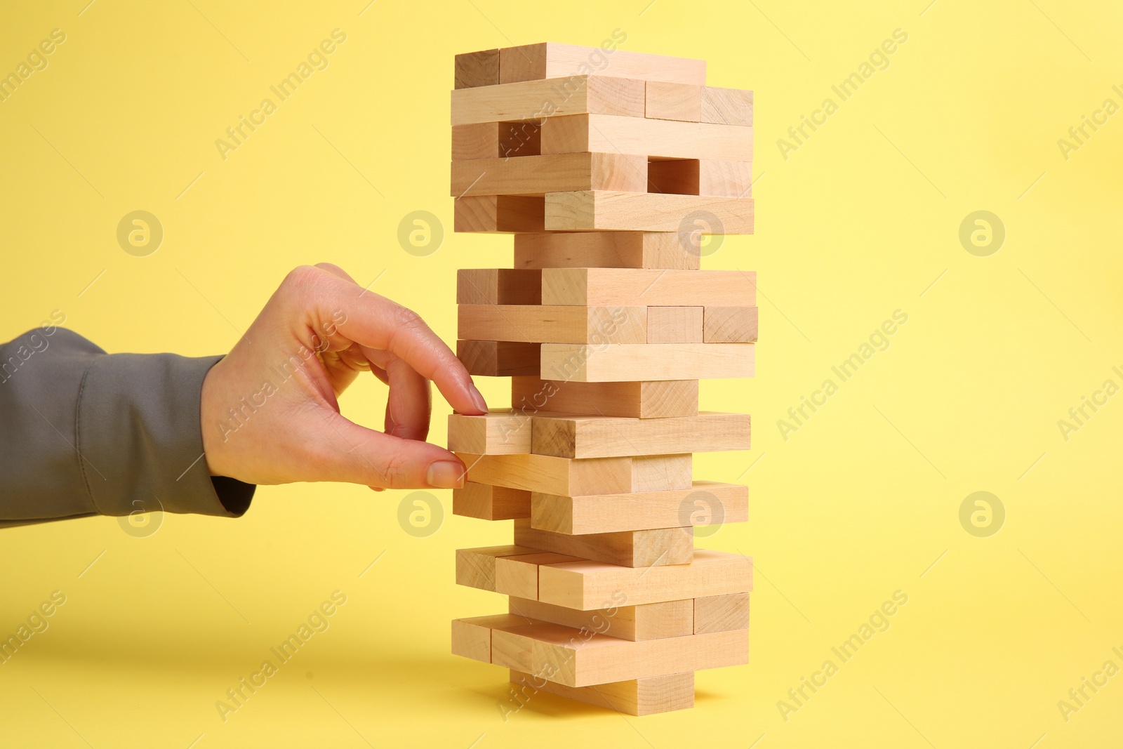 Photo of Woman playing Jenga tower on yellow background, closeup