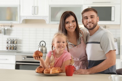 Photo of Happy family with freshly oven baked buns at table in kitchen. Space for text