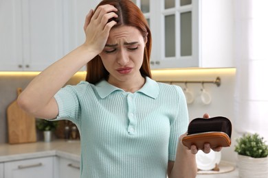 Upset woman with empty wallet at home