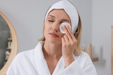 Photo of Young woman cleaning her face with cotton pad near in bathroom