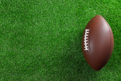 Photo of American football ball on green grass, top view. Space for text
