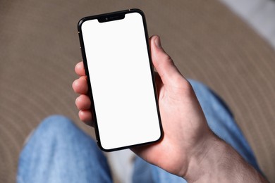 Man holding smartphone with blank screen indoors, closeup. Mockup for design