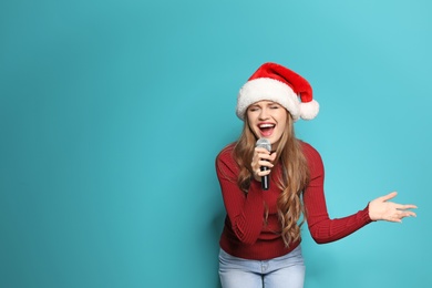 Young woman in Santa hat singing into microphone on color background. Christmas music
