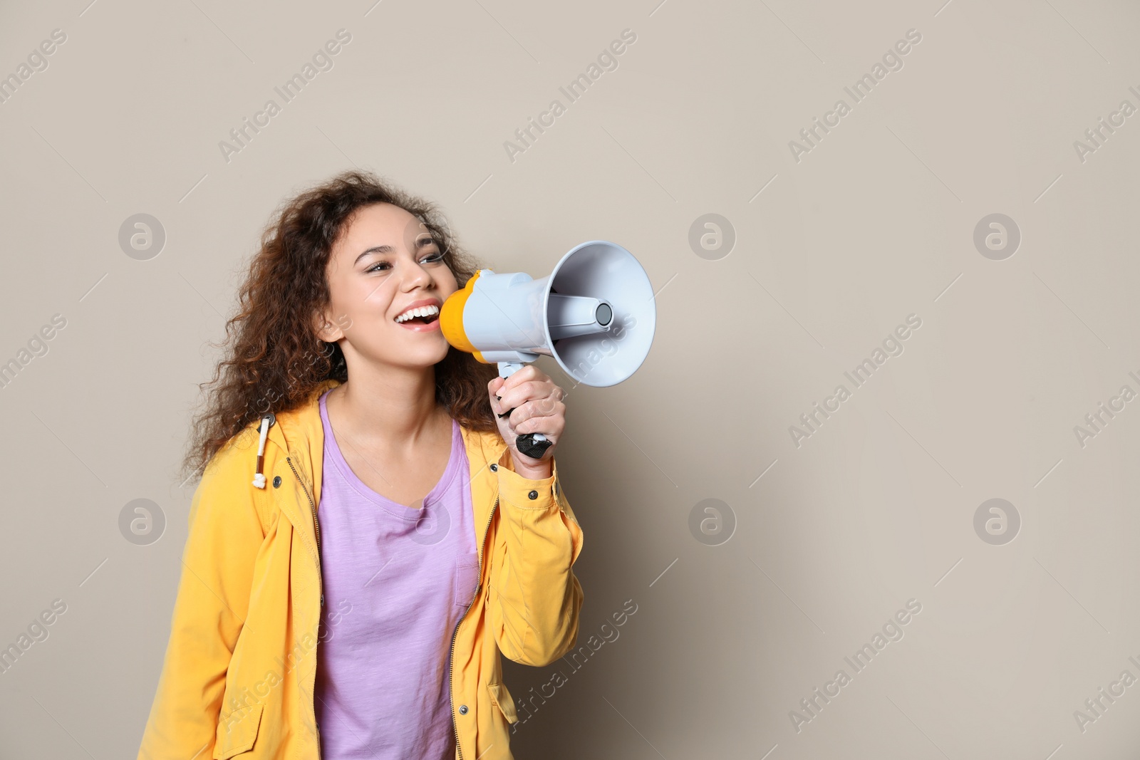 Photo of Young African-American woman with megaphone on color background. Space for text