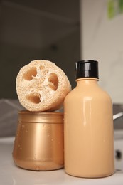 Photo of Natural loofah sponge and cosmetic products on washbasin in bathroom, closeup