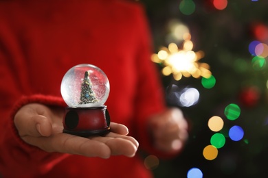 Photo of Woman holding snow globe on blurred background, closeup. Space for text