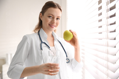 Nutritionist with glass of water and apple near window in office