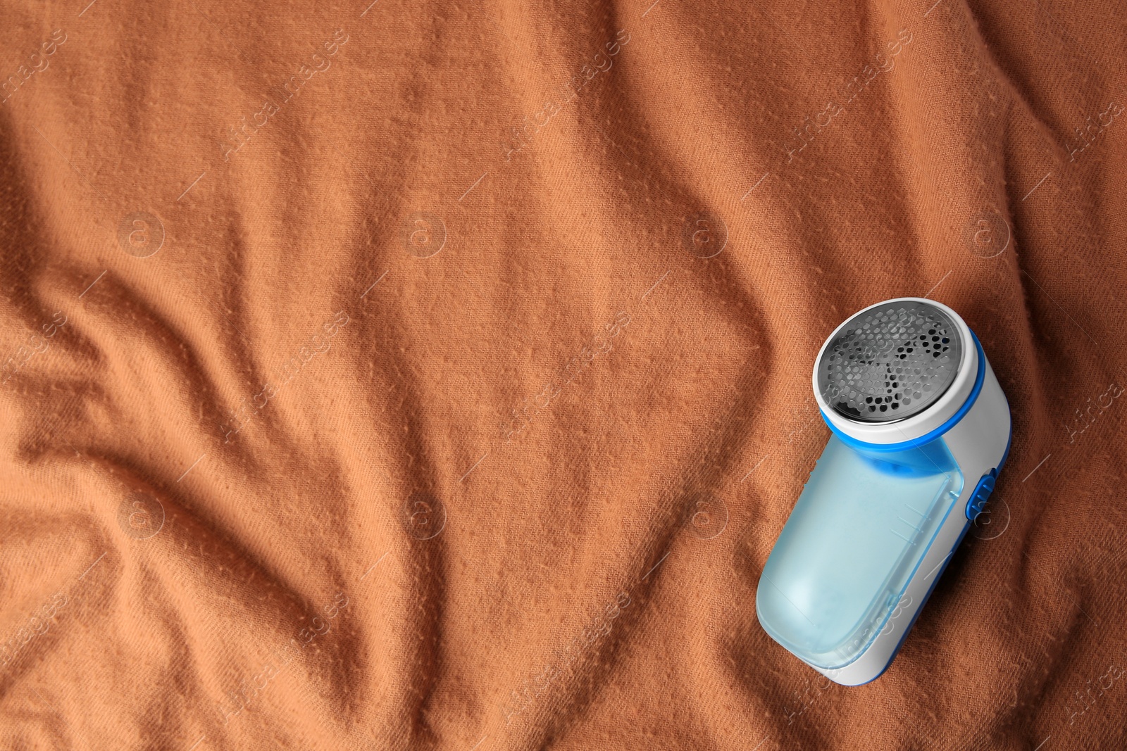 Photo of Fabric shaver on brown cloth with lint, top view. Space for text