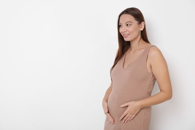 Beautiful pregnant woman in beige dress on white background, space for text