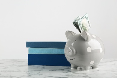 Photo of Piggy bank with dollars and books on table against white background