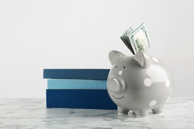 Piggy bank with dollars and books on table against white background