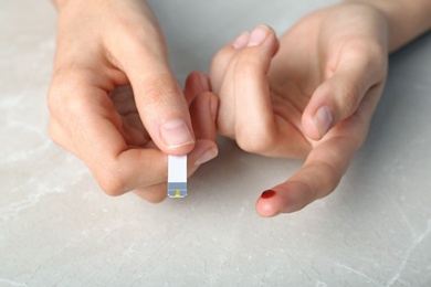 Photo of Woman with blood sugar test stripe at table. Diabetes control